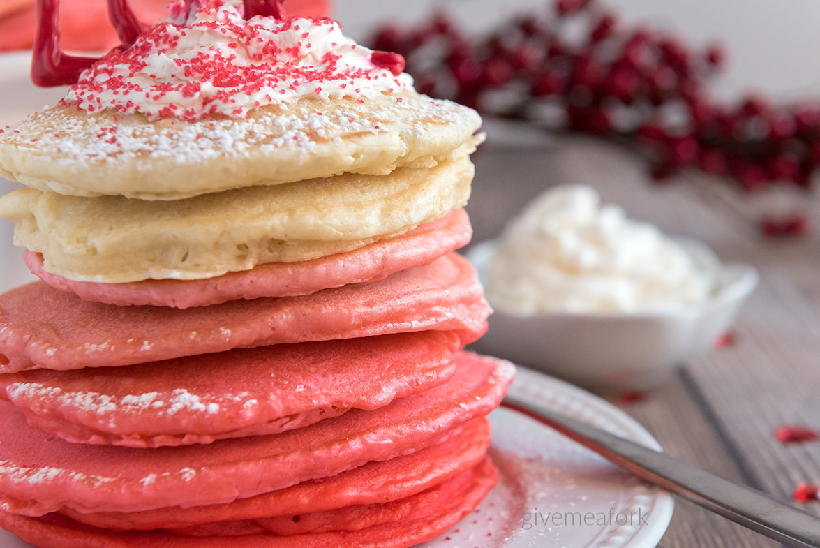 a short stack of pink pancakes with whipped cream on a white plate 