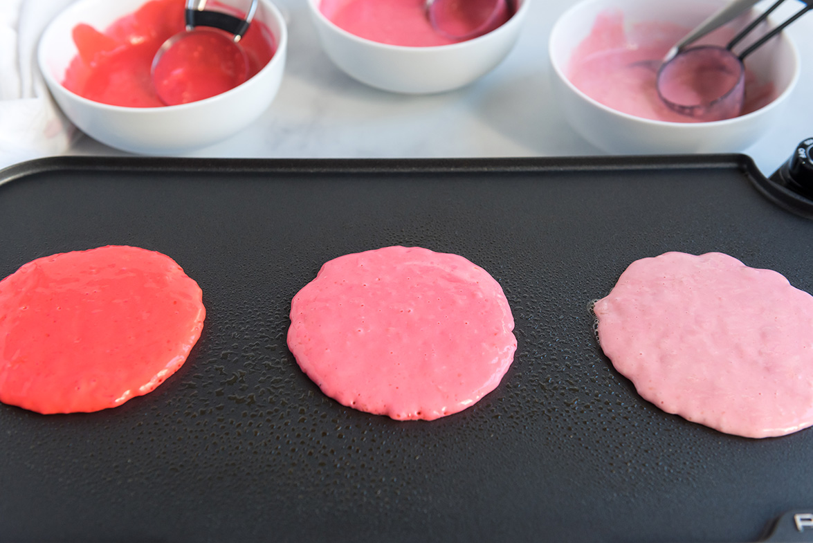 3 pink pancakes on a black electric griddle 