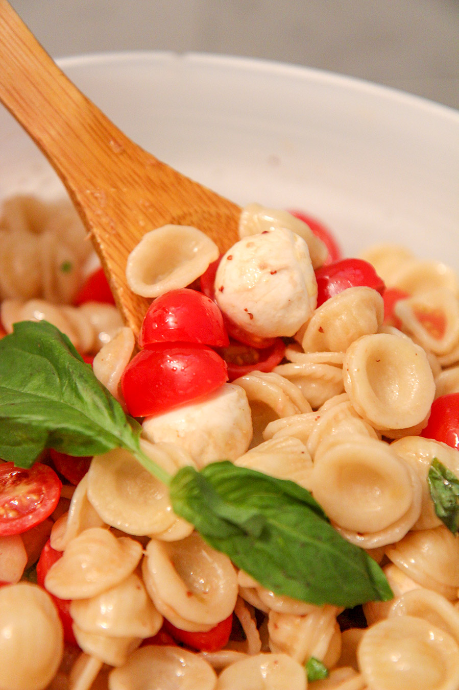 Caprese pasta salad in a white bowl with a wooden spoon.