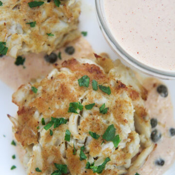 two lump crab cakes with parsley on top and a side of remoulade in a small bowl.