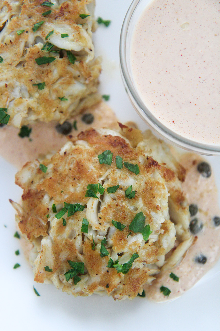 two lump crab cakes with parsley on top and a side of remoulade in a small bowl.