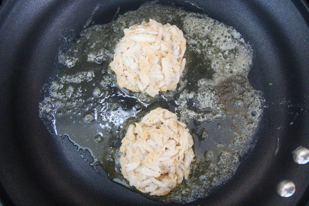 two crab patties in a greased black skillet.