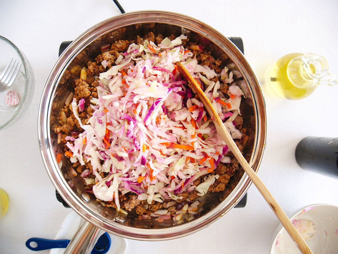 cooked pork and cabbage with a wooden spoon in a skillet.