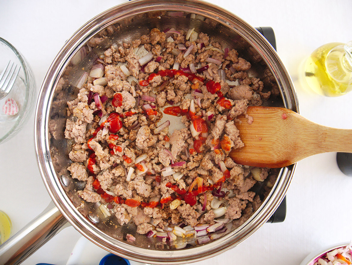 cooked pork with sriracha sauce and a wooden spoon in a skillet.