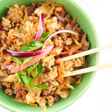 pork, cabbage, red onions, cilantro, and chop sticks in a green bowl.