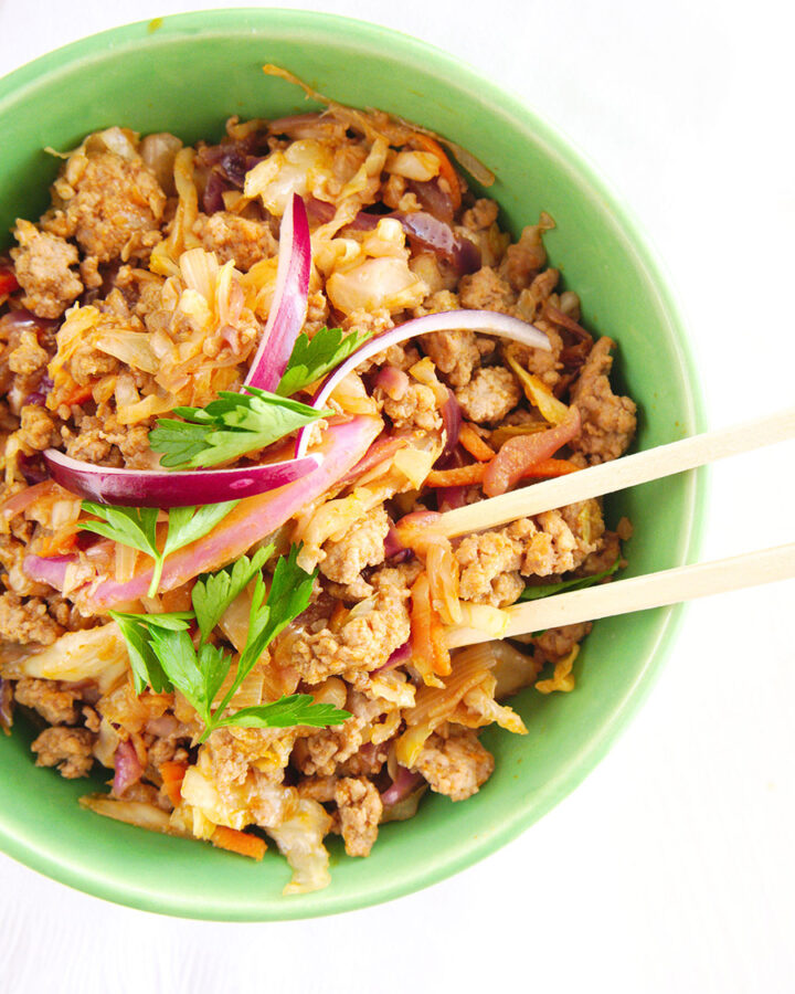 pork, cabbage, red onions, cilantro, and chop sticks in a green bowl.