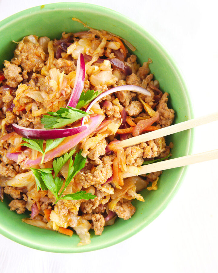 pork, cabbage, red onions, cilantro, and chop sticks in a green bowl.