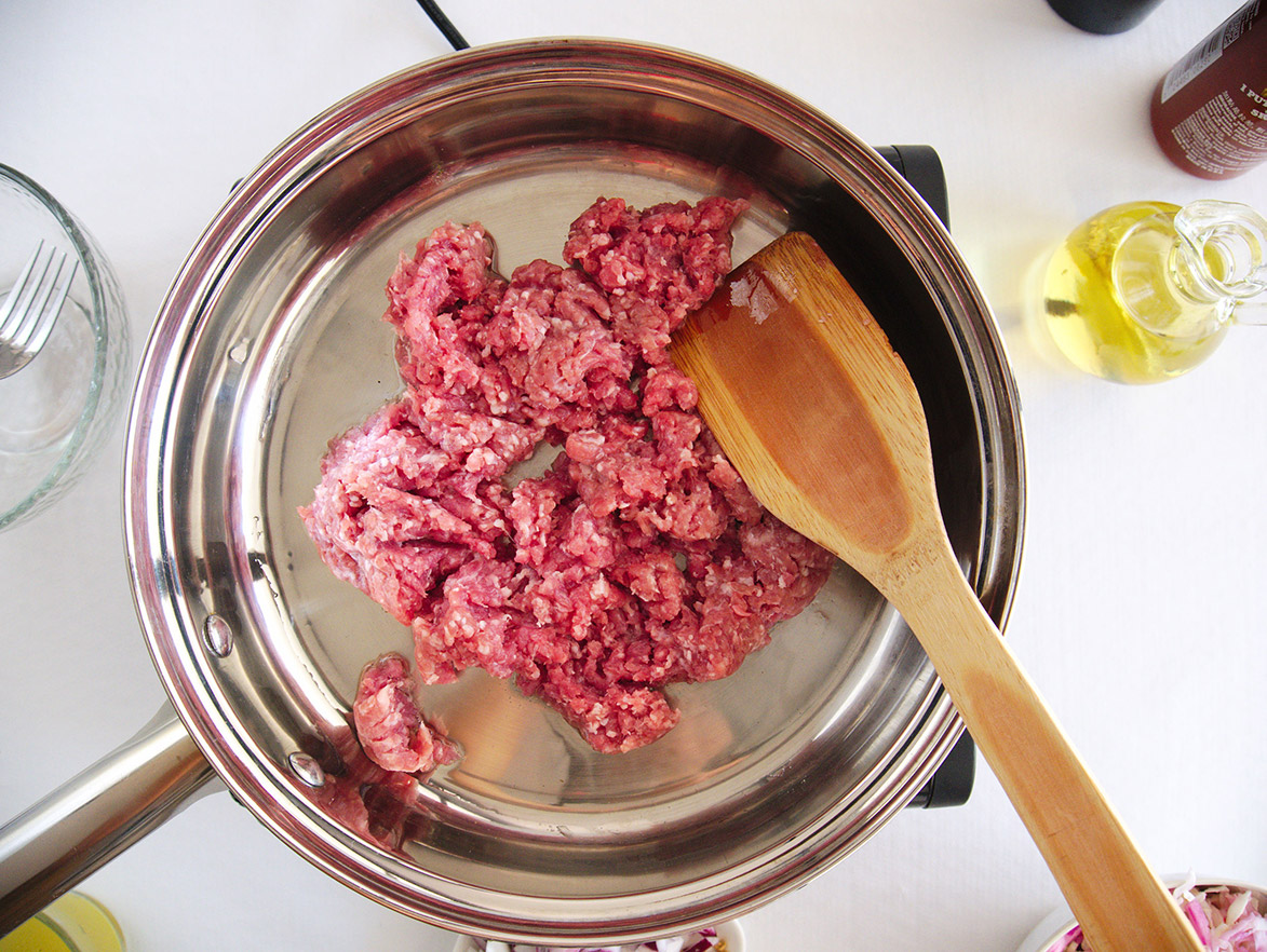 ground raw pork and a wooden spoon in a skillet.