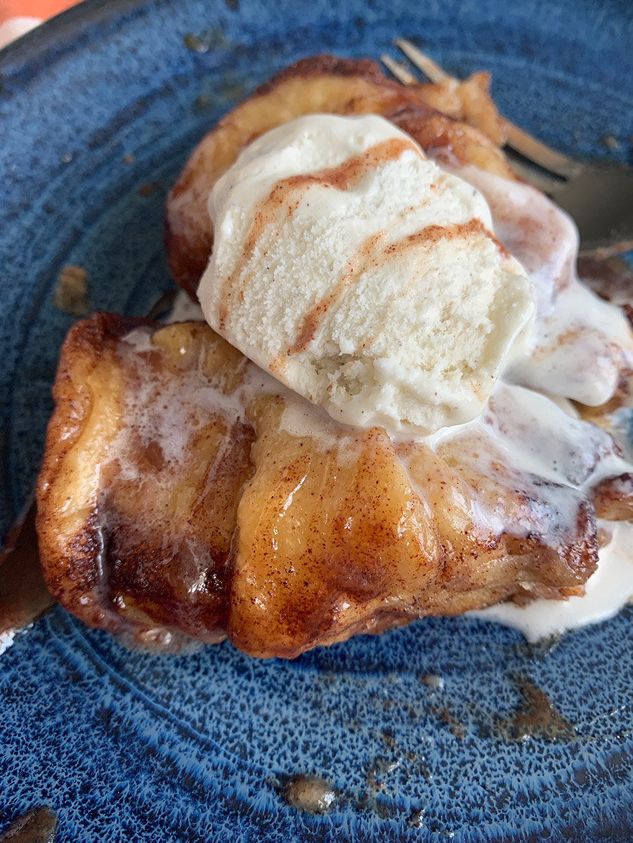 an up close shot of apple dumplings with sauce and vanilla ice cream on a small blue plate.