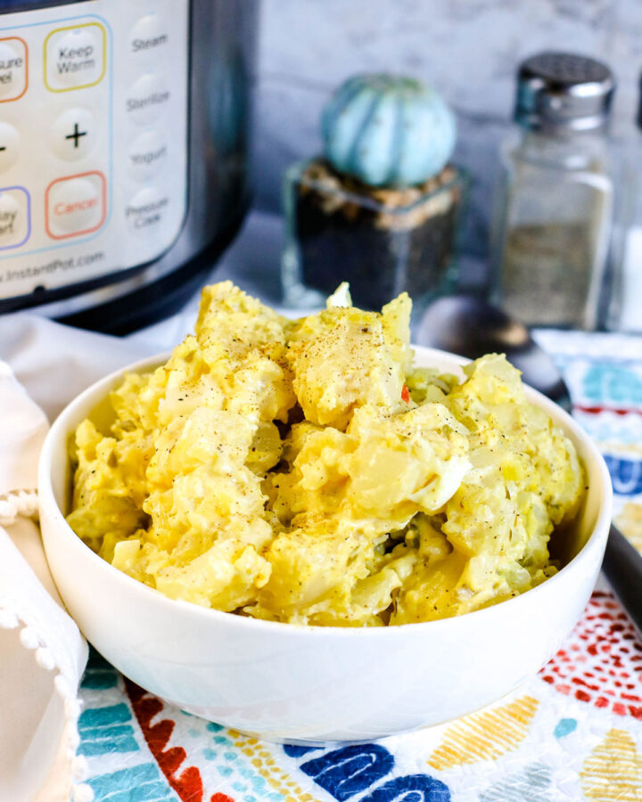 potato salad in a small white bowl with an instant pot and salt shakers in the background.