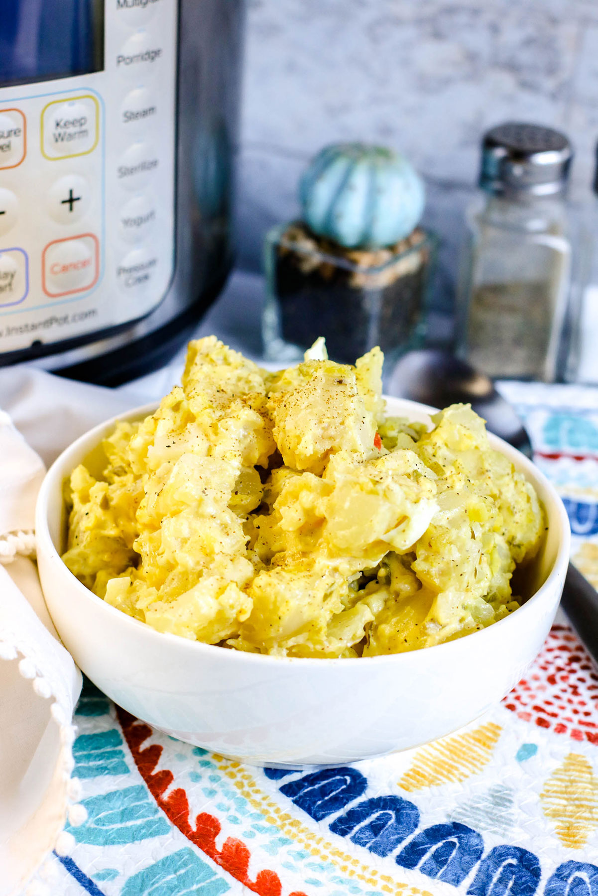 potato salad in a small white bowl with an instant pot and salt shakers in the background. 