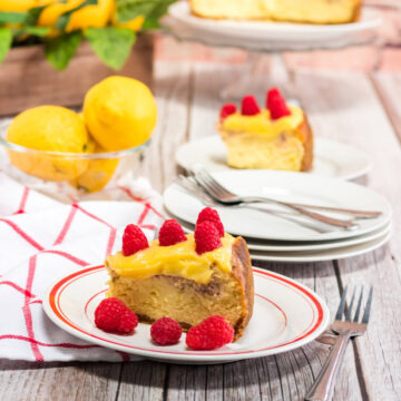 a slice of instant pot raspberry lemonade cheesecake on a white and red plate with a fork, towel, and lemons on the side.