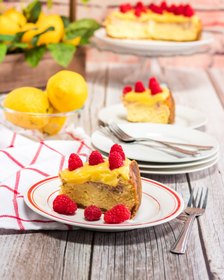 a slice of instant pot raspberry lemonade cheesecake on a white and red plate with a fork, towel, and lemons on the side.