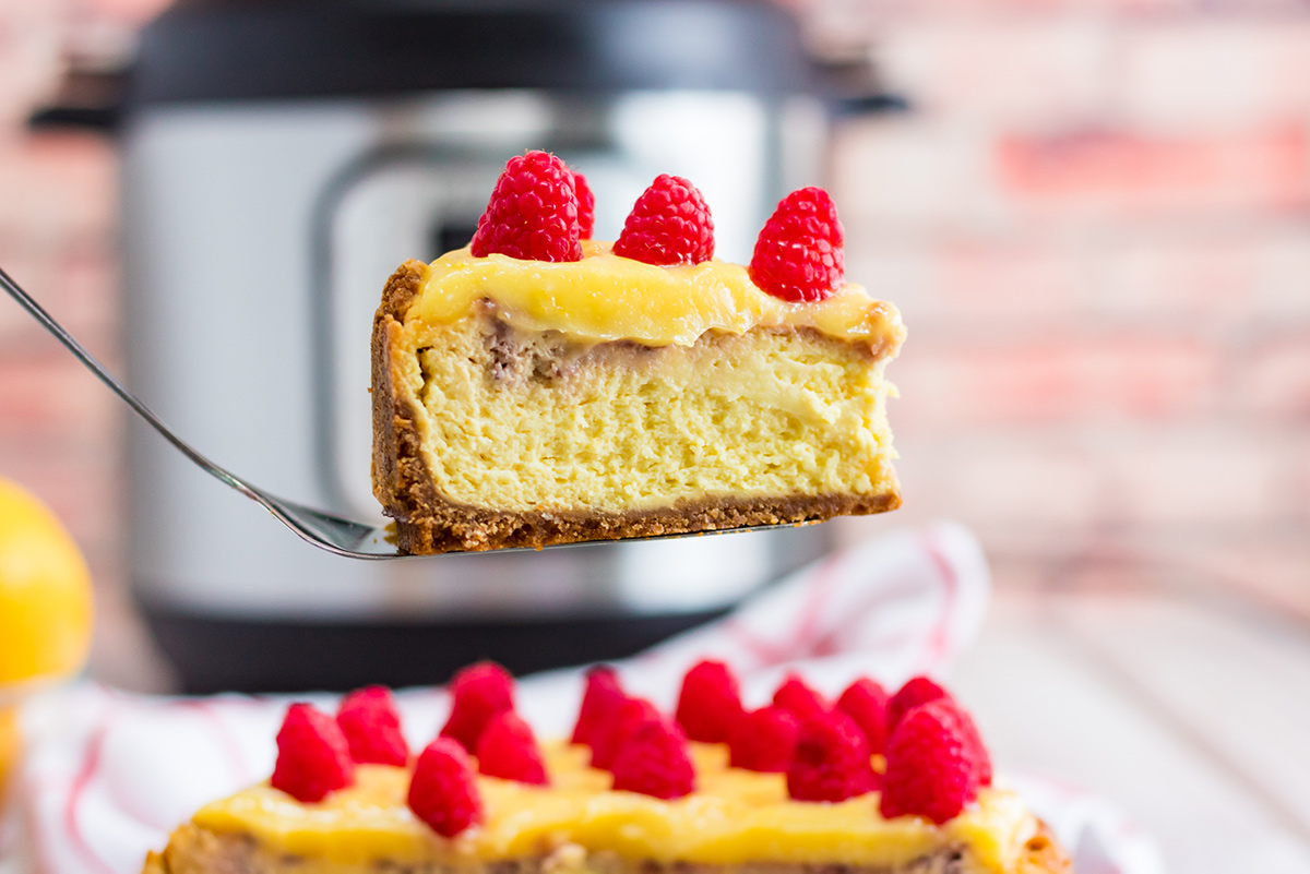 a slice of cheesecake with raspberries on top and an instant pot in the background. 