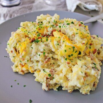 loaded cauliflower bake on a gray plate with salt shakers on the side and a green casserole in the background.