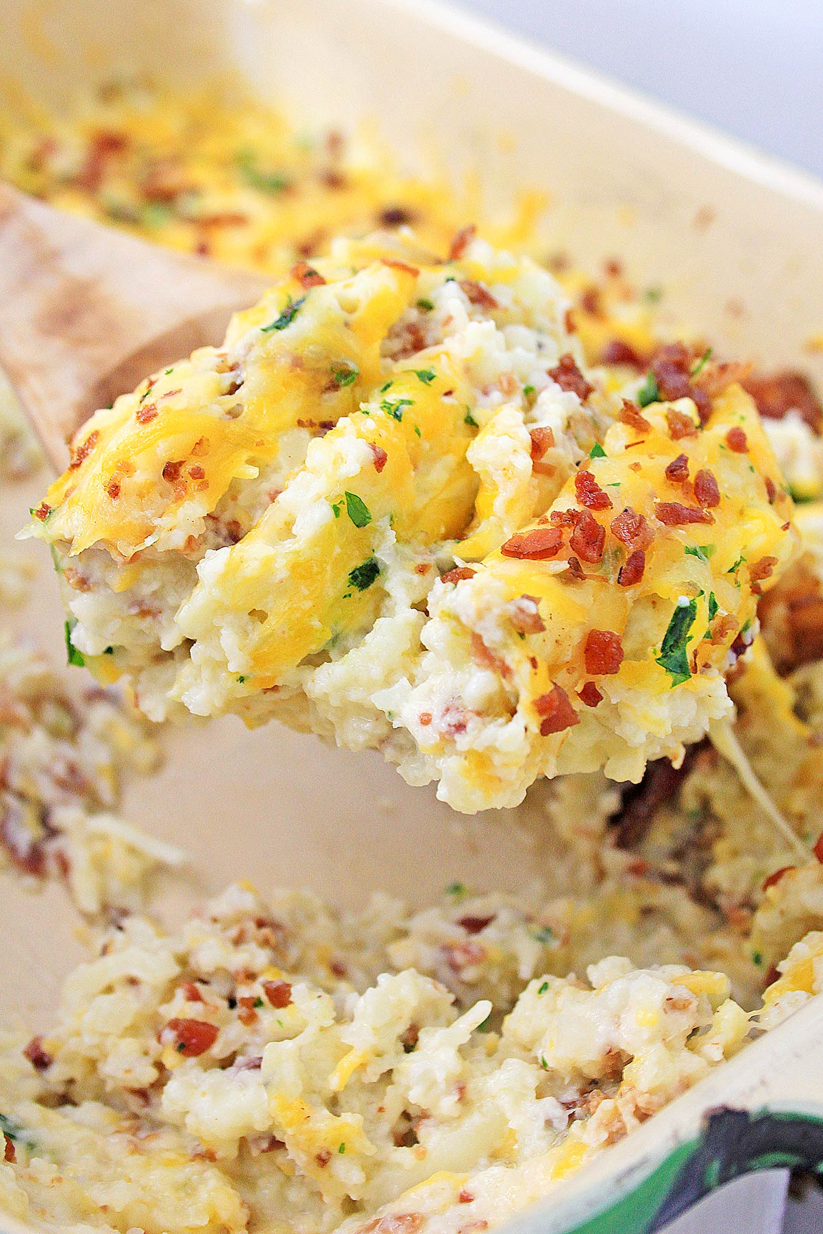 a spoon lifting a portion of cheesy cauliflower rice out of a casserole dish. 