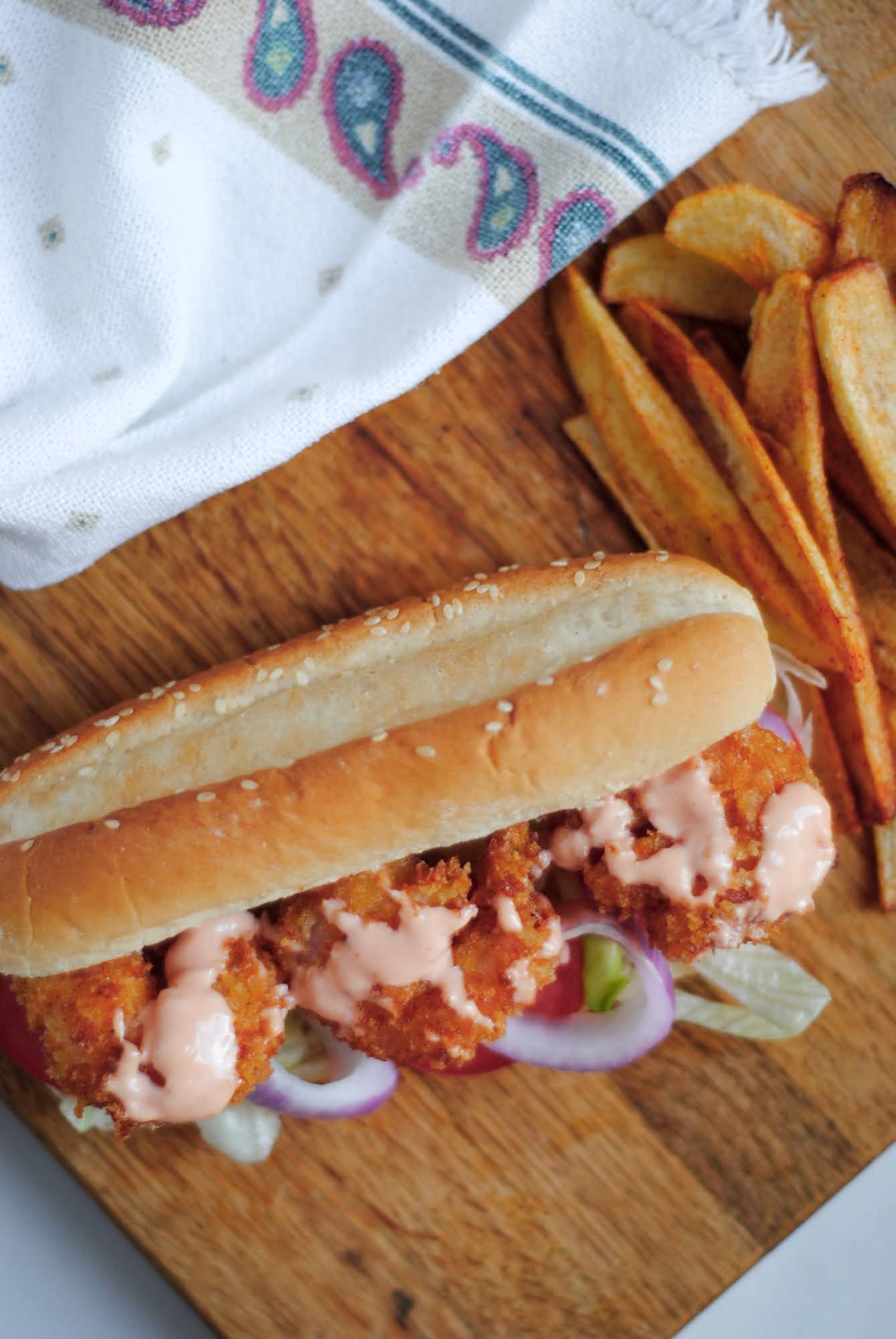 shrimp po'boy sandwich on a wooden board with french fries and a towel on the side.