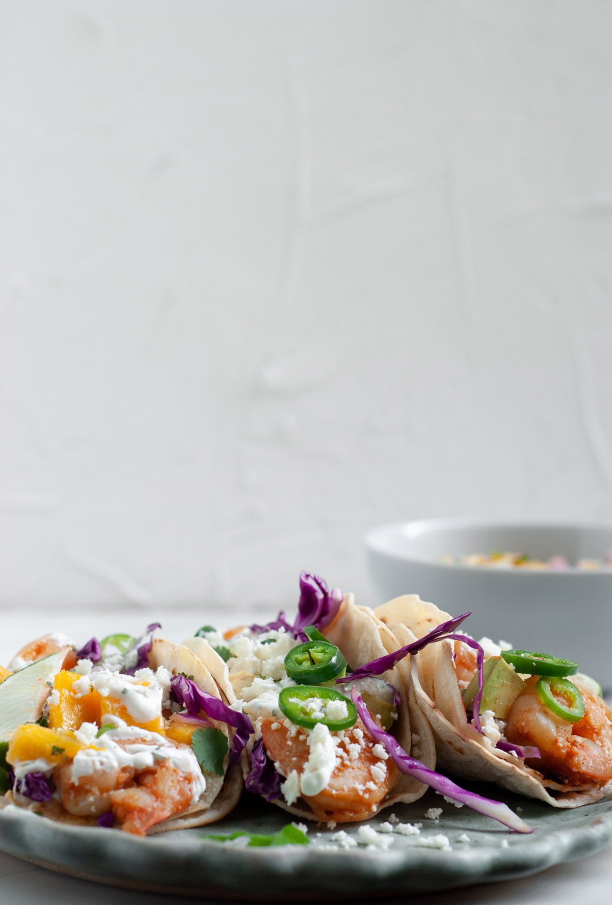 Three tacos on a blue plate with a small white bowl on the side and a white back drop. 