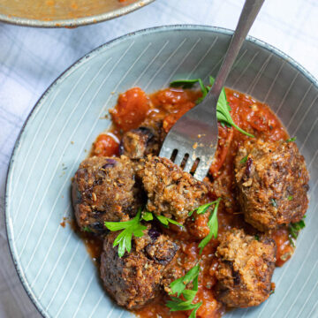 five lentil vegetarian meatballs with marinara sauce and parsley in a light blue bowl with a fork.