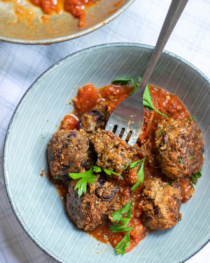 five lentil vegetarian meatballs with marinara sauce and parsley in a light blue bowl with a fork.