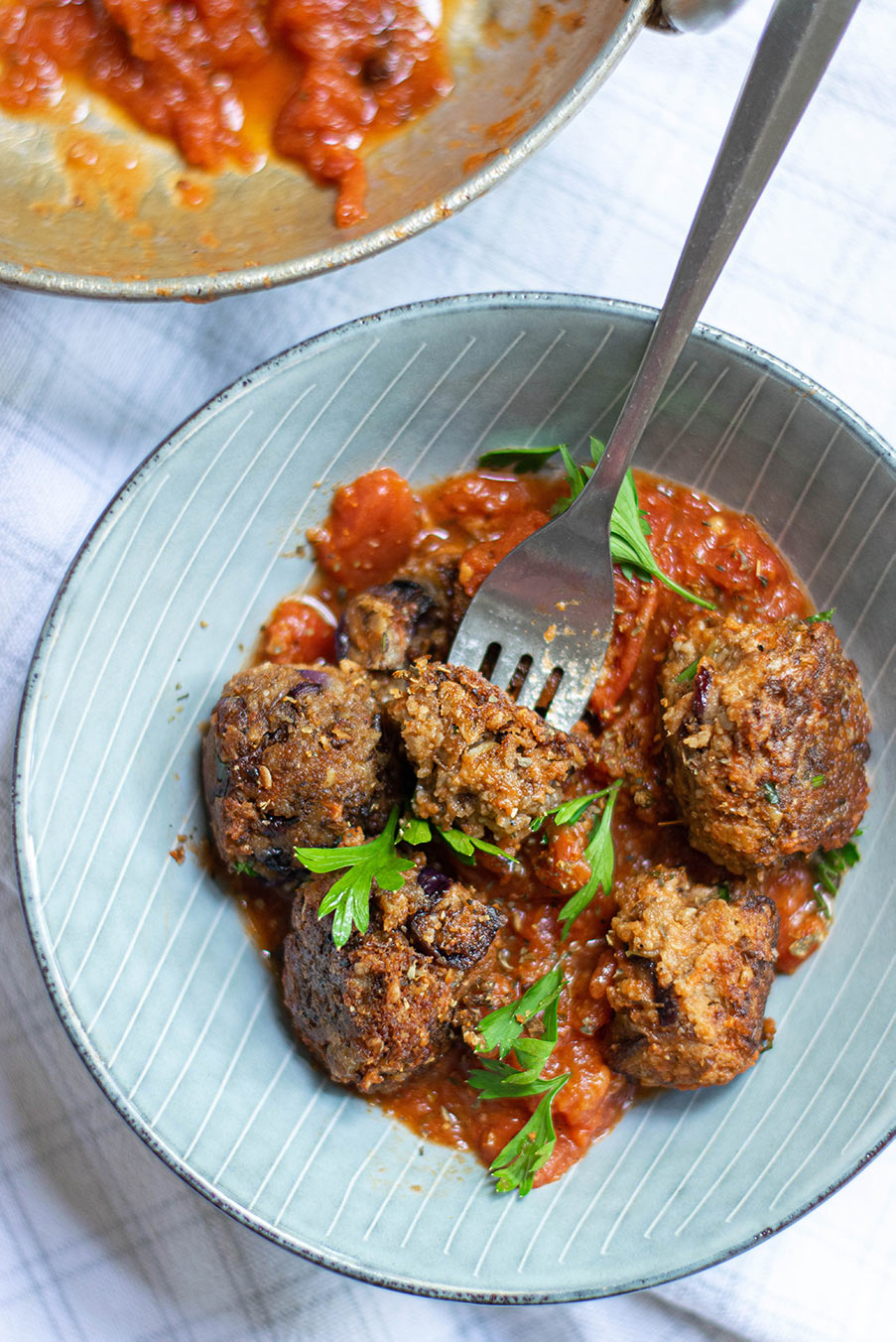 five lentil vegetarian meatballs with marinara sauce and parsley in a light blue bowl with a fork. 