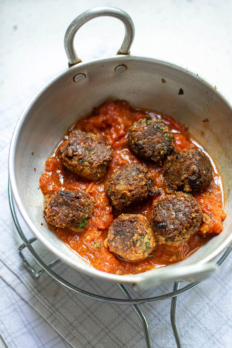 seven vegan meatballs over marinara sauce in a skillet with handles. 