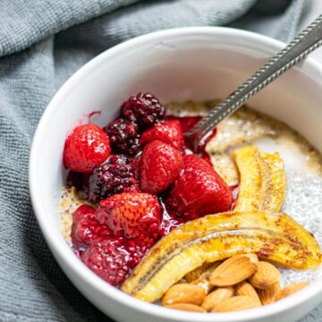 a white bowl with oats, berries, bananas, nuts, and a spoon. A blue towel on the side.