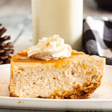 a slice of eggnog cheesecake with caramel and whipped cream on top and milk in the background.