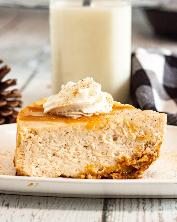 a slice of eggnog cheesecake with caramel and whipped cream on top and milk in the background.