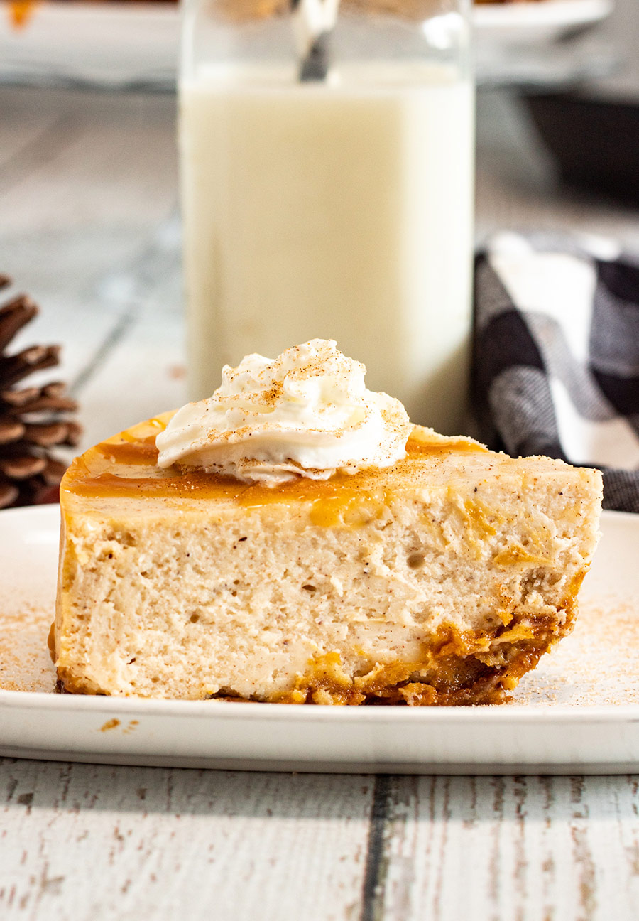 a slice of eggnog cheesecake with caramel and whipped cream on top and milk in the background. 