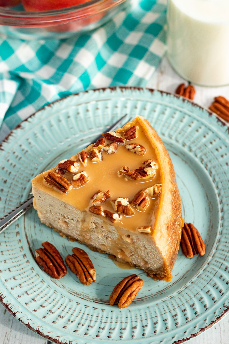 a slice of instant pot salted caramel apple cheesecake on a blue plate with a glass of milk on the side.