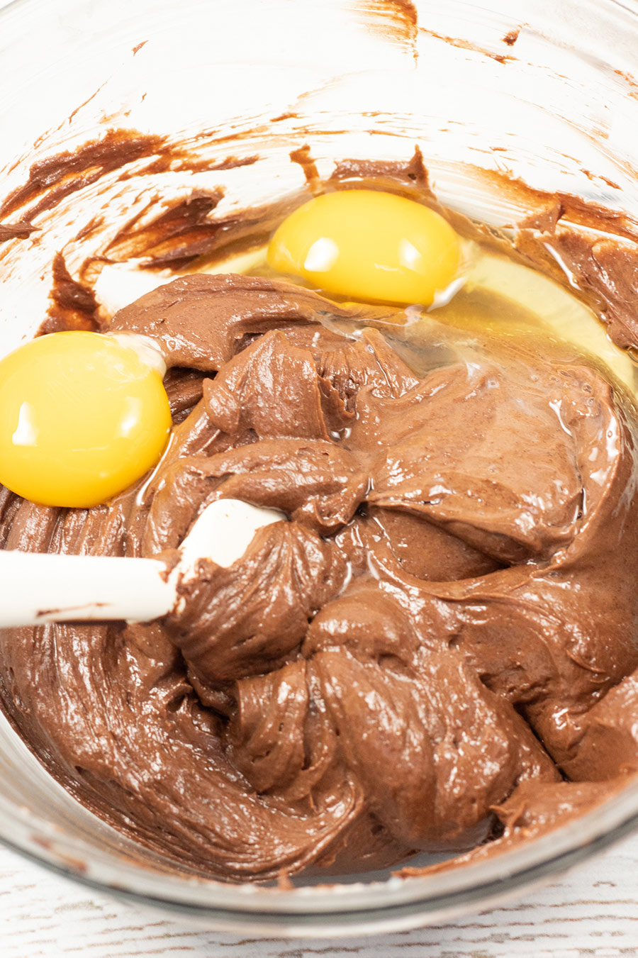 chocolate cheesecake filling in a bowl with two eggs and a spatula. 