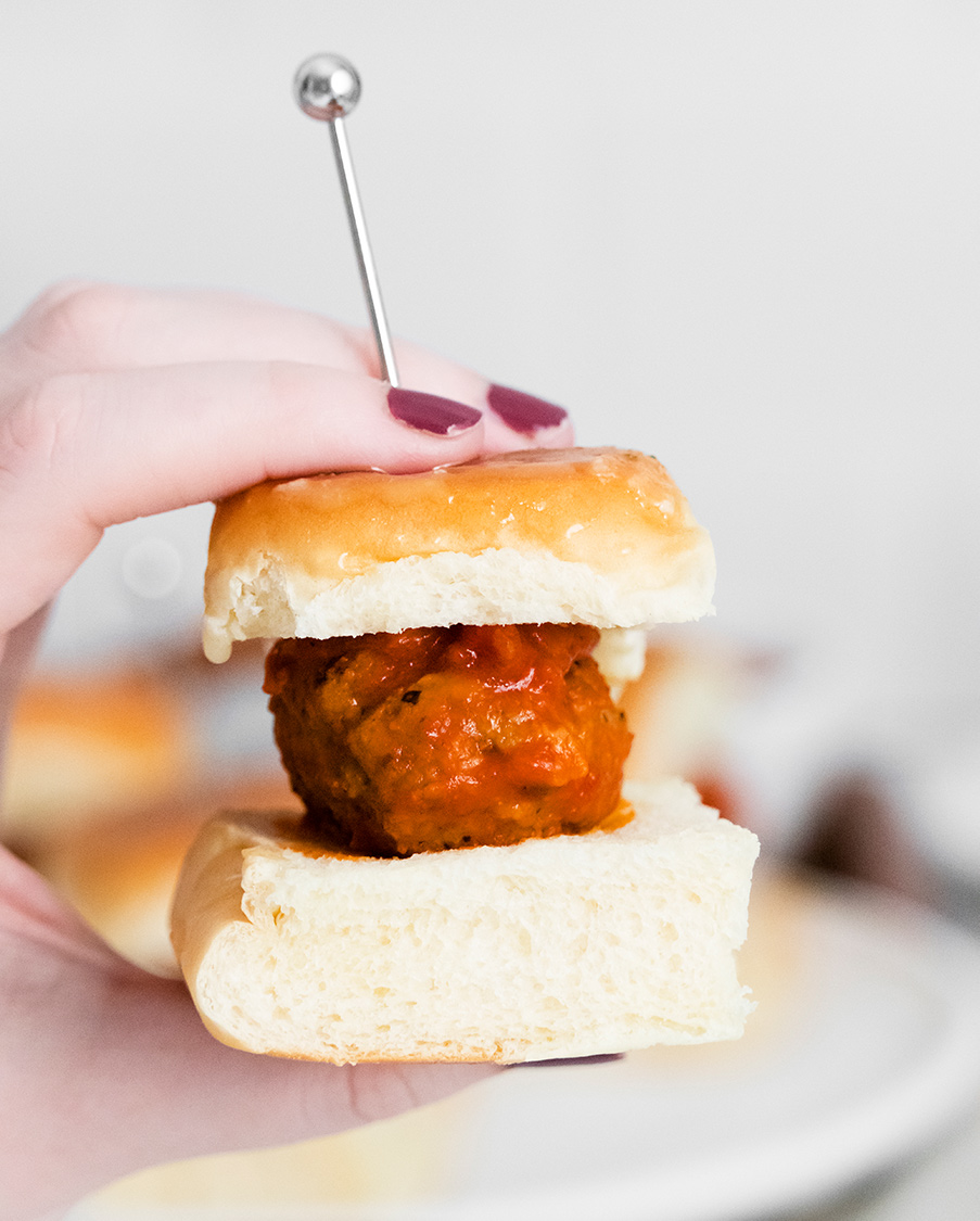 a hand holding a meatball slider up close. 