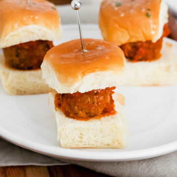 three meatball sliders on a white plate.