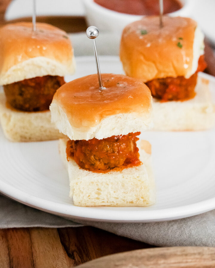 three meatball sliders on a white plate.