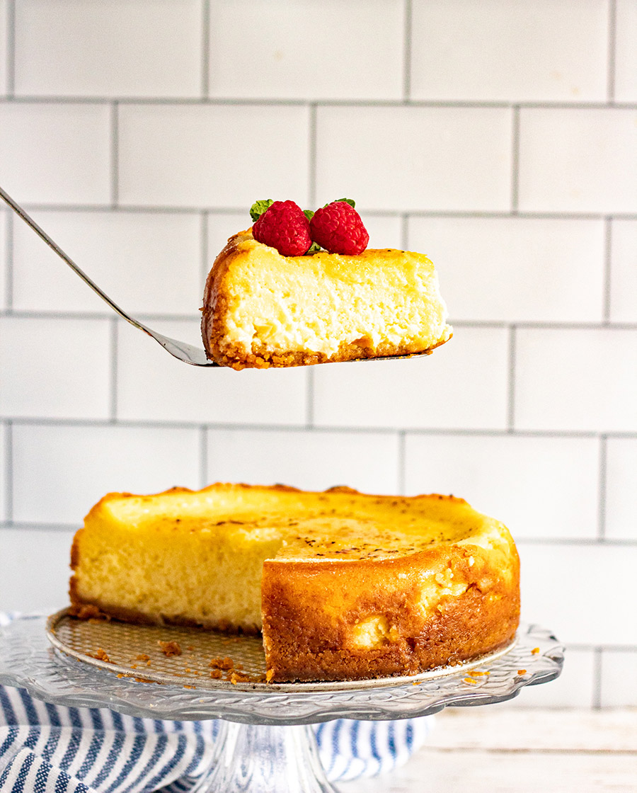 a spatula lifting a slice of cheesecake over an entire cake. 