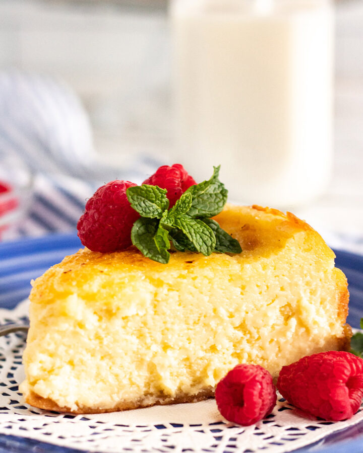 a slice of creme brulee cheesecake up close with raspberries, mint, and a glass of milk in the background.