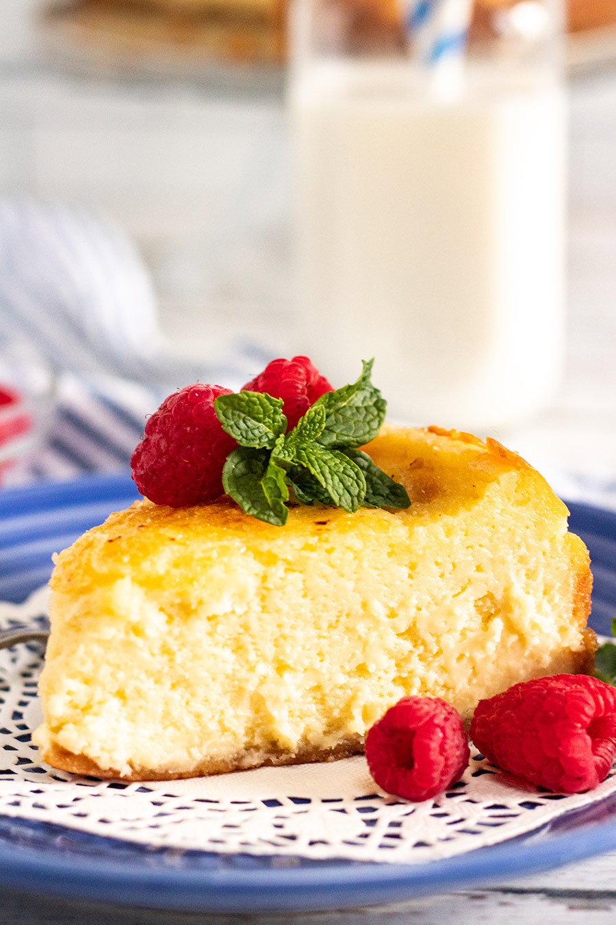 a slice of creme brulee cheesecake up close with raspberries, mint, and a glass of milk in the background.