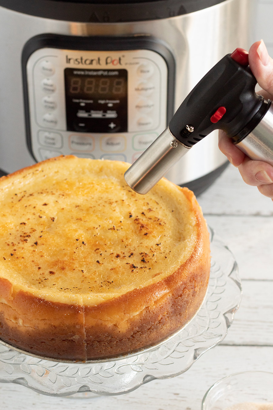 blow torch, an instant pot in the background, and an entire cheesecake.