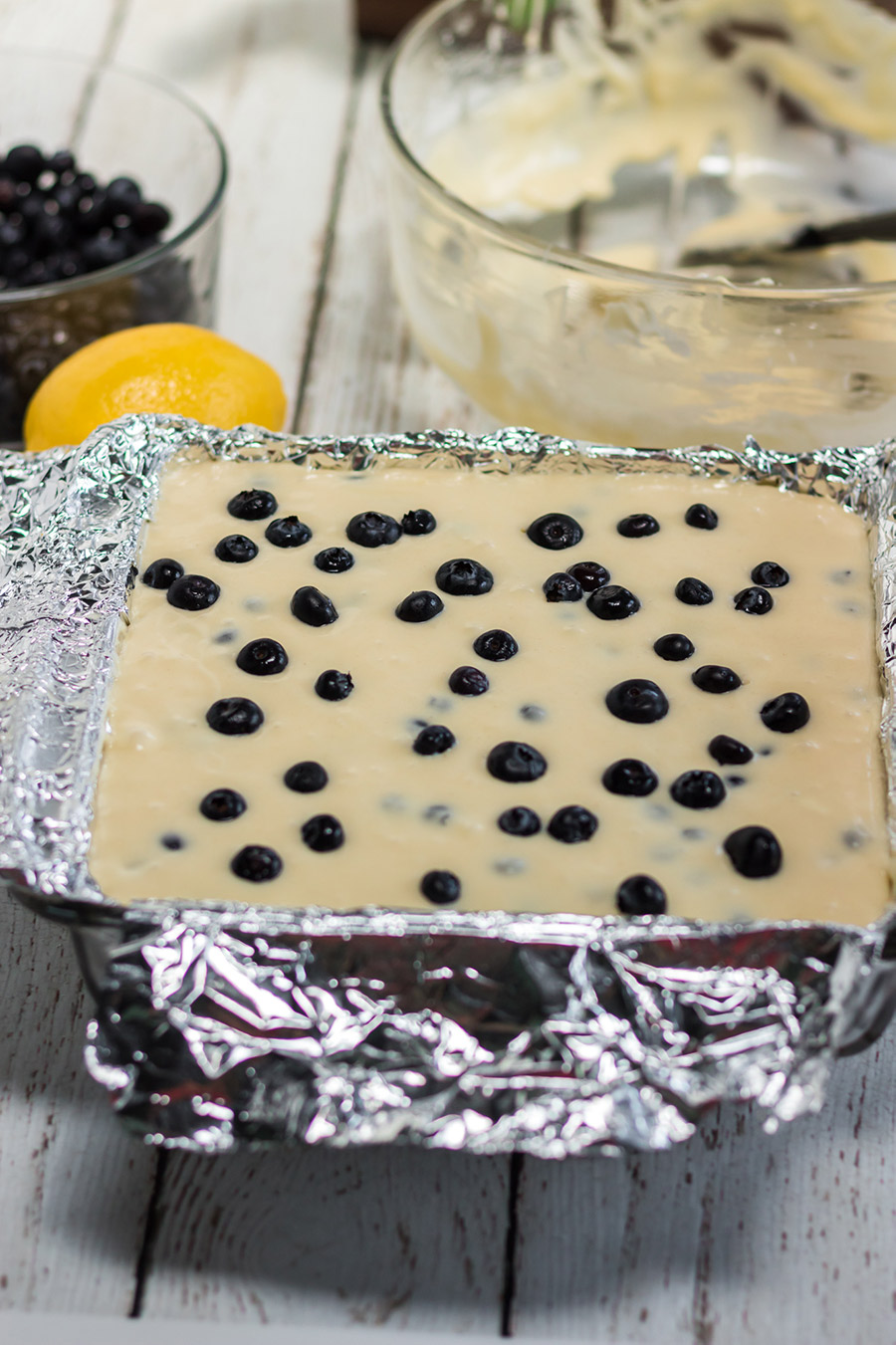 lemon cream filling in a baking dish with fresh blueberries on top and aluminum foil around the edges. 