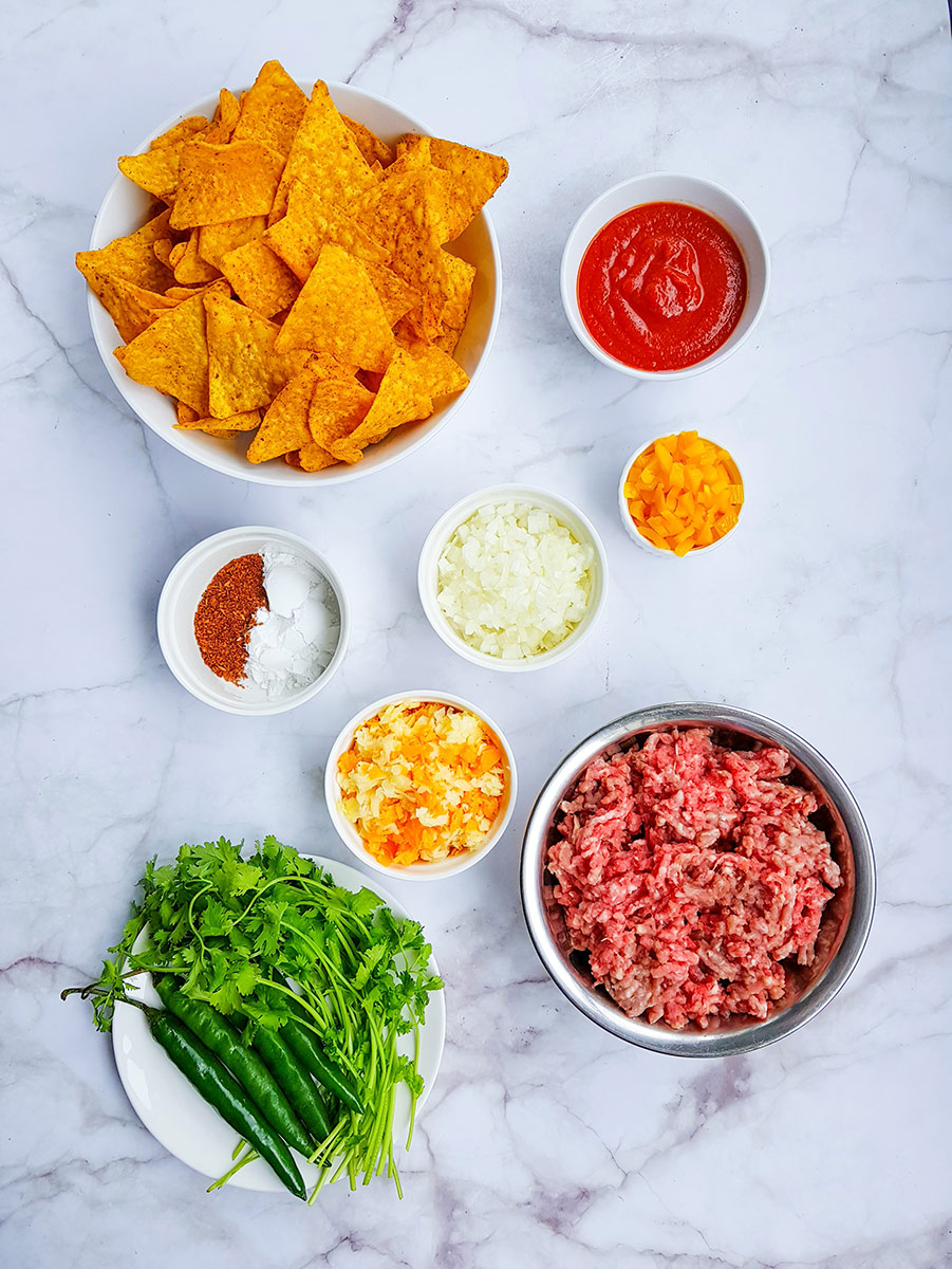 doritos, sauce, raw ground beef, cheese, green herbs, spices, and onions. 