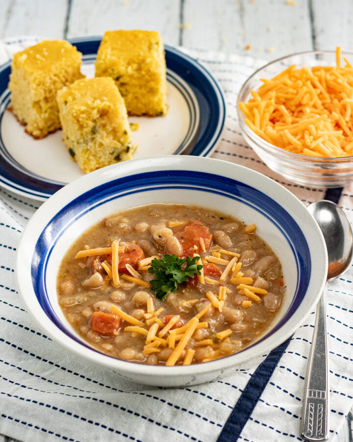 bean and bacon soup in a bowl with corn bread and cheese in the background.