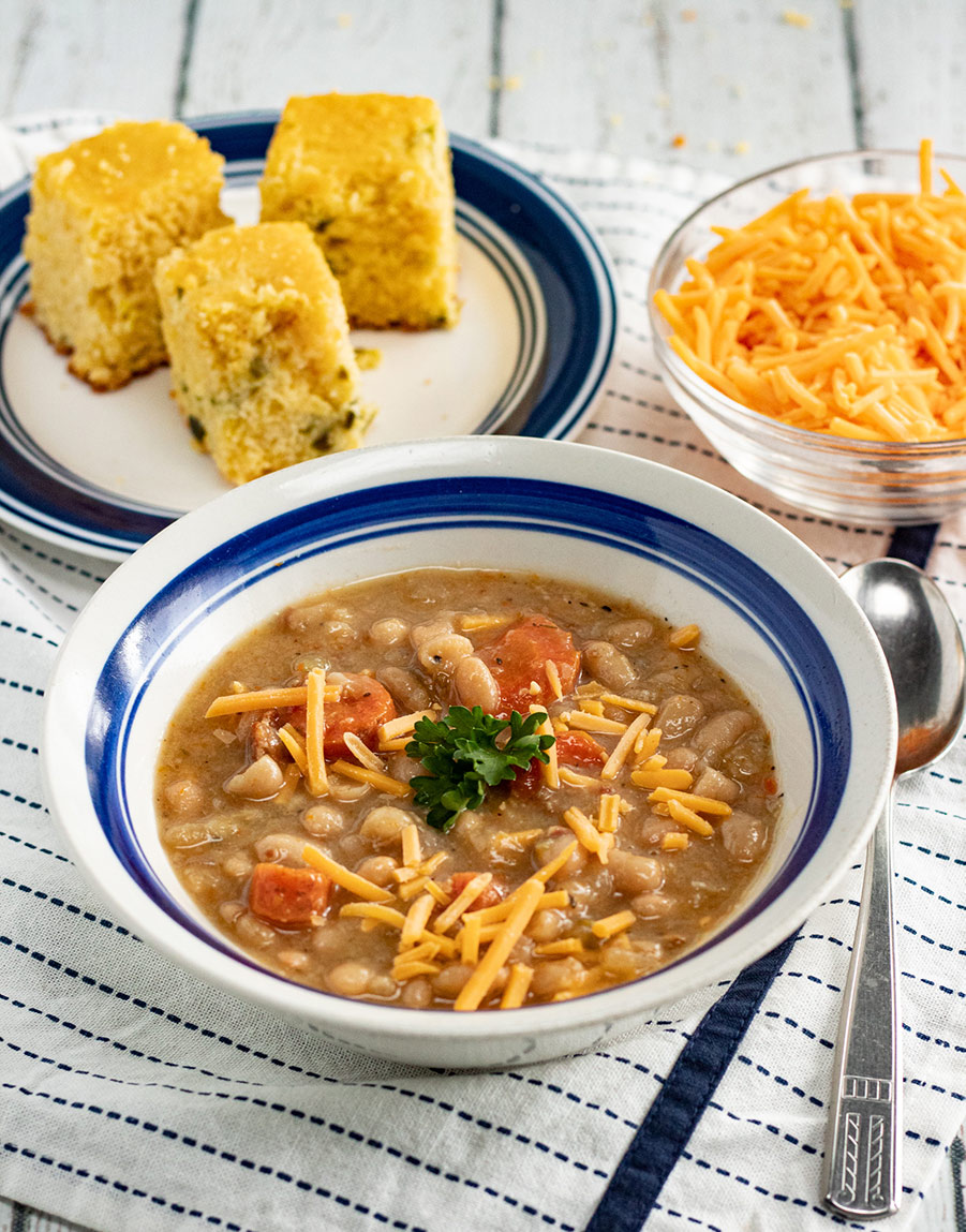 bean and bacon soup in a bowl with corn bread and cheese in the background.