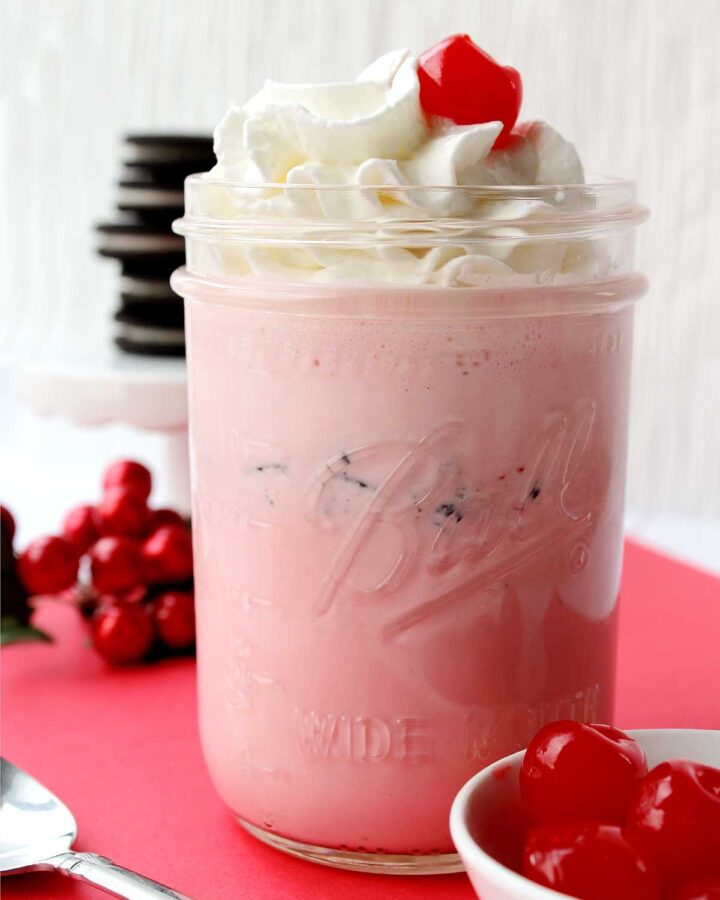 pink strawberry oreo milkshake with whipped cream and a cherry on top.