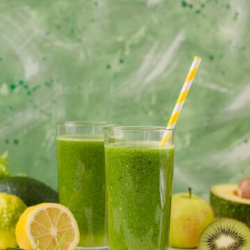 two kiwi smoothies in glasses with fruits on the side.