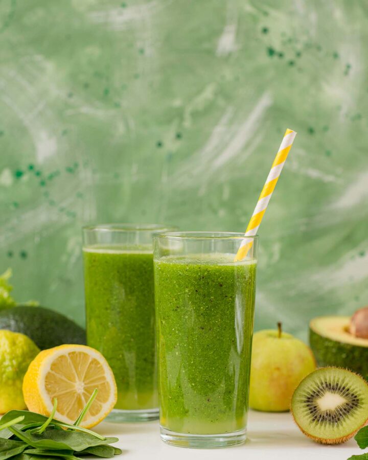 two kiwi smoothies in glasses with fruits on the side.