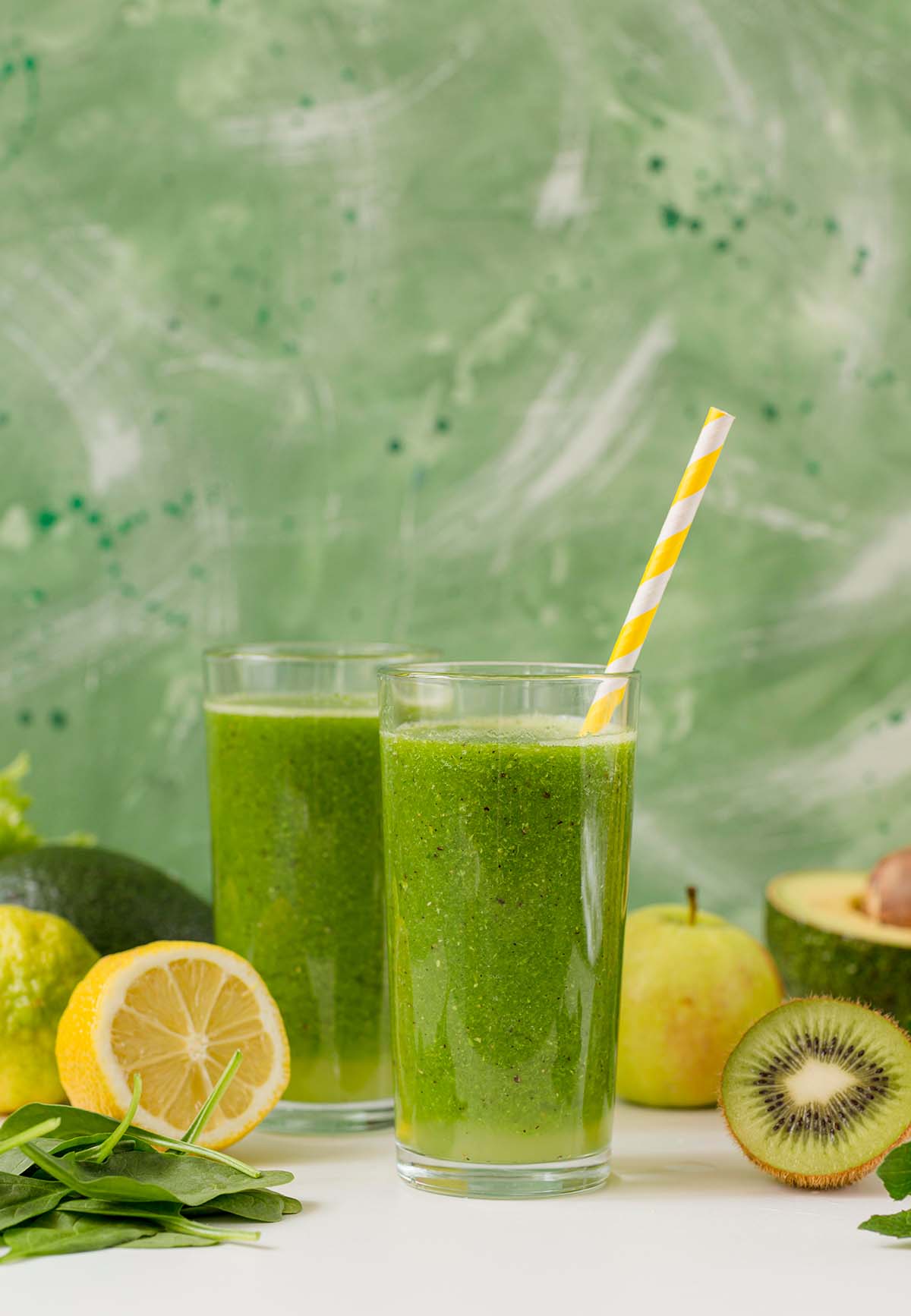 two kiwi smoothies in glasses with fruits on the side.