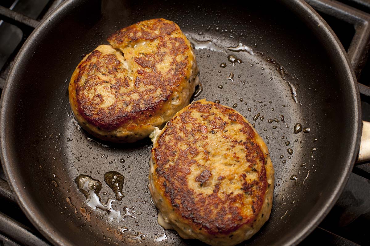Two crab cakes frying in a skillet. 