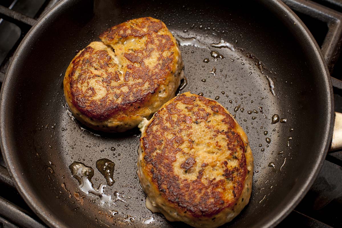 Two crab cakes frying in a skillet.