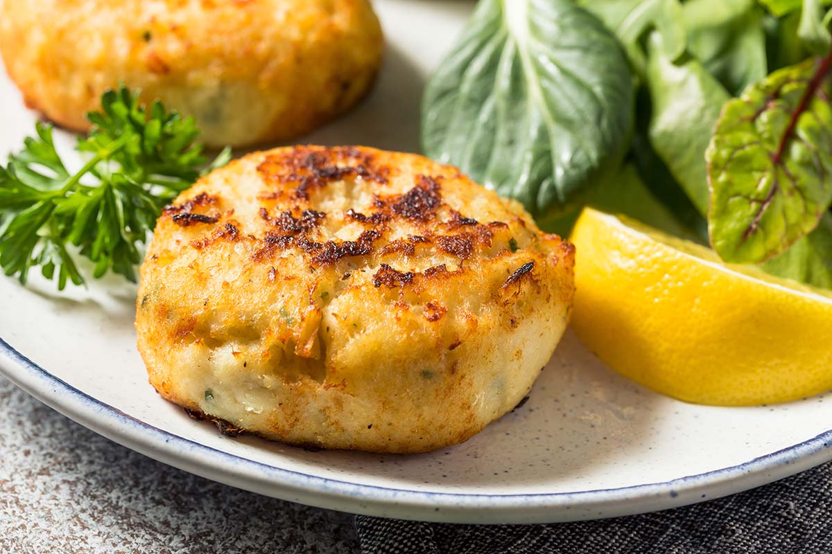 Two crab cakes on a plate with a lemon wedge and salad. 